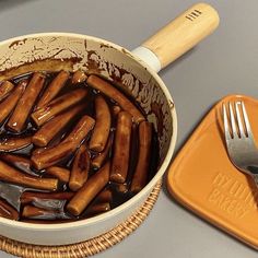 there is a pot full of hot dogs and a fork in the bowl next to it