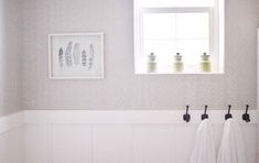 two towels hanging on hooks in front of a window with white walls and wood flooring