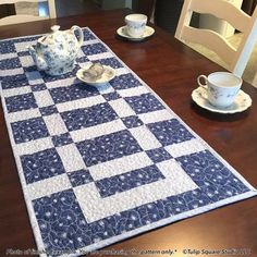 a blue and white quilted table runner on a wooden table with teacups