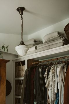 an open closet with clothes hanging from the ceiling and a lamp on top of it