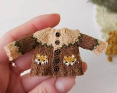 a hand holding a small knitted sweater ornament in it's palm