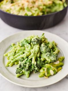 broccoli on a white plate next to a skillet filled with cheese and sauce