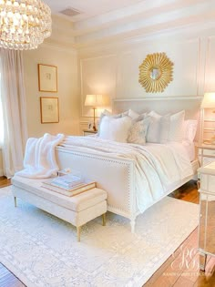 a white bed sitting in a bedroom on top of a hard wood floor next to a chandelier