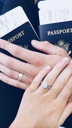 two people are holding their hands together while wearing wedding rings and matching engagement bands, with passports in the background