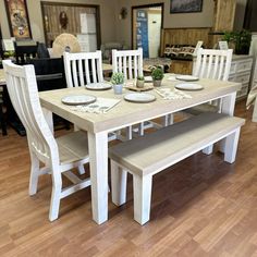 a dining room table with white chairs and plates on the bench in front of it