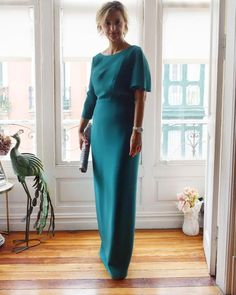 a woman standing in front of a window wearing a blue dress