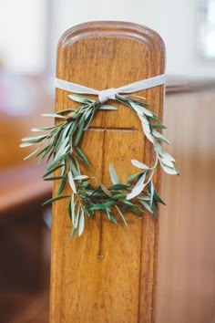 an olive wreath tied to the back of a wooden church pew during a wedding ceremony