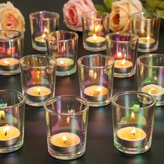 many small glass cups with lit candles in them on a table next to some roses