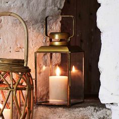 two lit candles sitting next to each other in front of a brick wall and basket