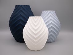 three different colored vases sitting next to each other on a gray surface in front of a grey background