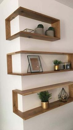 three wooden shelves on the wall with plants and candles in them, one is empty