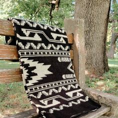 a black and white blanket sitting on top of a wooden bench next to a tree