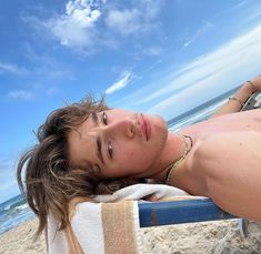 a woman laying on top of a beach next to the ocean under a blue sky