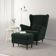 a green chair and ottoman in a white room with a lamp on the side table