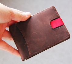 a hand holding a brown wallet with a red strip