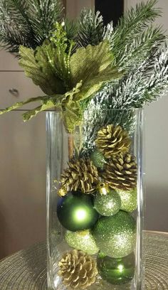 a clear vase filled with green ornaments and pine cones on top of a round table