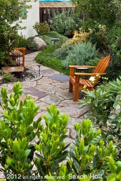 two wooden benches sitting next to each other on a stone walkway in front of a house