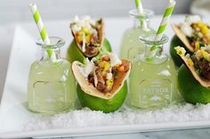 some tacos and drinks are sitting in small glass bottles on a white platter