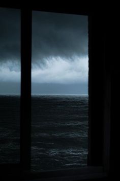 an ocean view from a window with dark clouds in the sky and water behind it