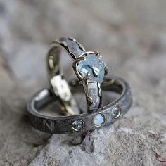 two wedding rings with blue topazte and diamond accents on them sitting on a rock