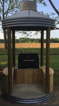 a grill sitting on top of a wooden bench under a gazebo next to a field