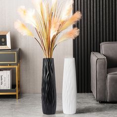 two tall vases with feathers in them on a marble floor next to a couch