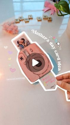 a person holding up a sticker with the image of a polaroid camera on it