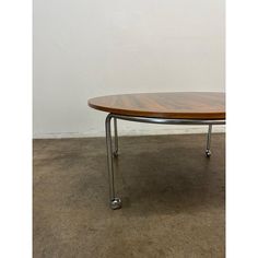 a wooden table sitting on top of a floor next to a white wall with metal legs