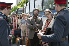 a group of people standing around each other in front of a bus and another man with glasses on his head