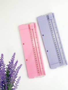 two rulers next to purple flowers on a white surface