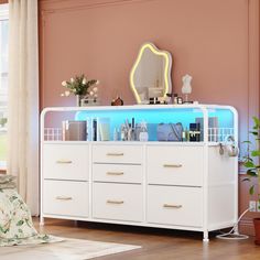 a white dresser with blue lights on the top and drawers below it in a pink room