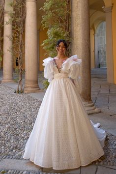 a woman in a white dress is standing on the stone walkway near pillars and trees