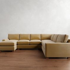 a beige sectional couch sitting on top of a wooden floor next to a white wall