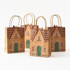 three brown paper bags with small houses on the front and one has green doors, two have windows