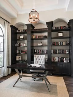 a home office with built - in bookcases and a leather chair under a chandelier