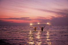 two people standing in the water with their arms up and one person raising their hands