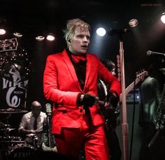 a man in a red suit playing guitar on stage