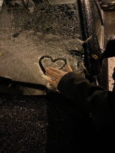 a person touching the side of a car with a heart drawn on it's windshield