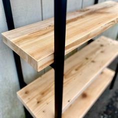 two wooden shelves sitting next to each other in front of a white wall and black metal frame