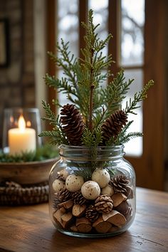 a glass jar filled with pine cones and eggs on top of a wooden table next to a candle