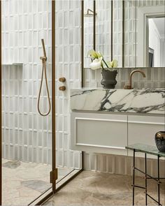 a bathroom with marble counter tops and white tile on the walls, along with a glass shower door