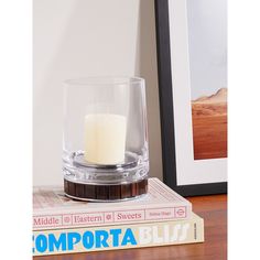 a glass candle holder sitting on top of a book next to a framed photograph and a wooden table