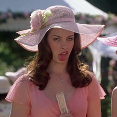 a woman in a pink dress and hat making a funny face