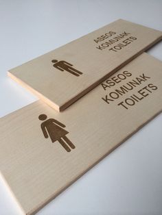 two wooden signs with the words asos kommak toilets and an image of a man holding a woman's hand