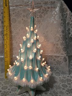 a small christmas tree with white lights on it's sides and a ruler in the background