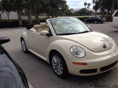 a beige convertible car parked in a parking lot next to other cars and palm trees