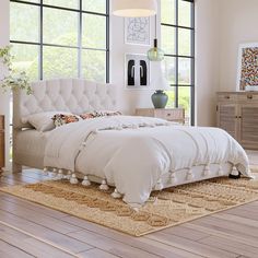 a bed with white linens and pillows in front of two large windows on the wall