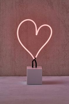 a heart shaped neon sign sitting on top of a white square box in front of a wall