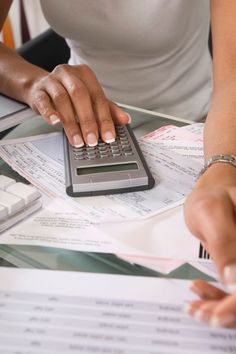 a woman is using a calculator on top of some papers and paperwork at a desk