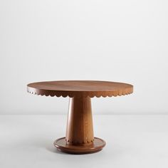 a round wooden table with scalloped edges and a circular base, on a white background